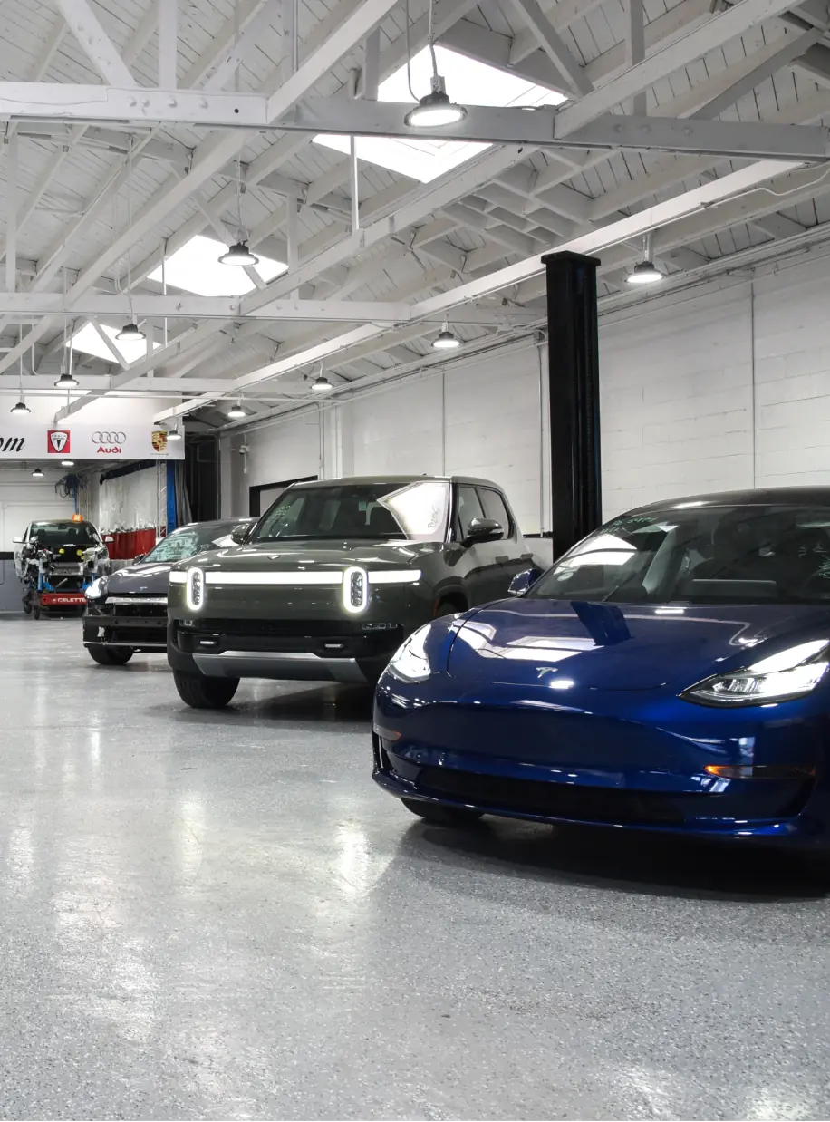 Three electric vehicles parked inside a well-lit industrial garage with a high ceiling and white walls.