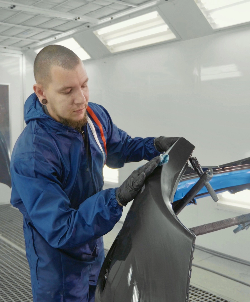 A person in a blue protective suit polishes a car part with a cloth in a workshop.