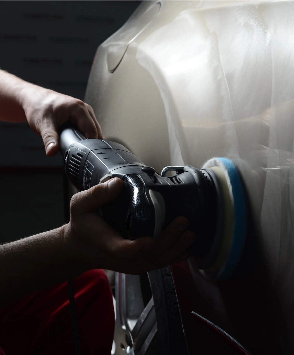 Hands using a power polisher on a car's surface, applying a smooth finish.