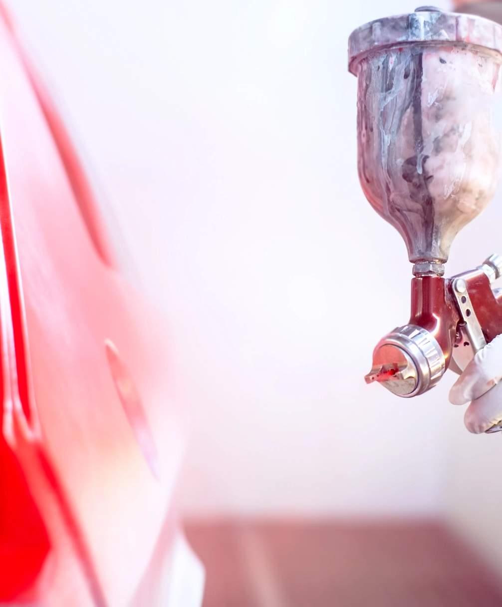 A person is using a spray gun to paint a car red in a workshop setting.