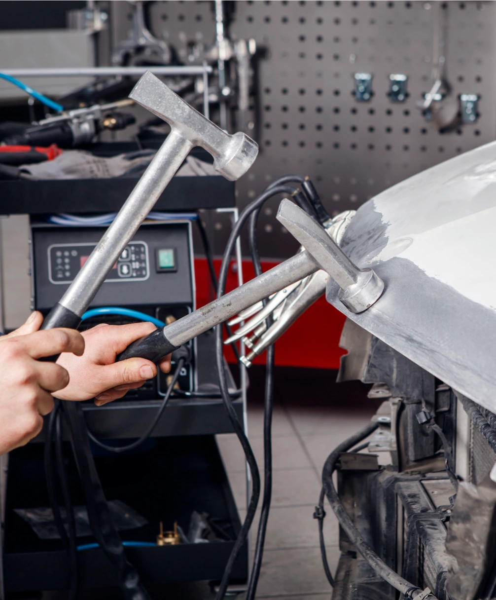 Mechanic uses two hammers to repair the dented body of a car in an auto repair shop.