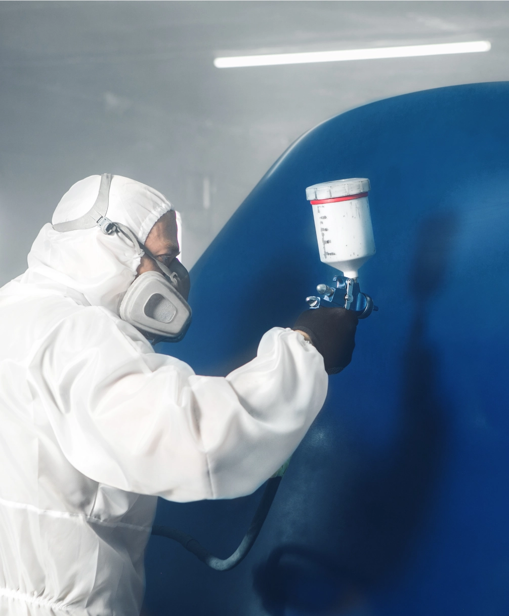 Person in protective gear spray-paints a large blue surface indoors.