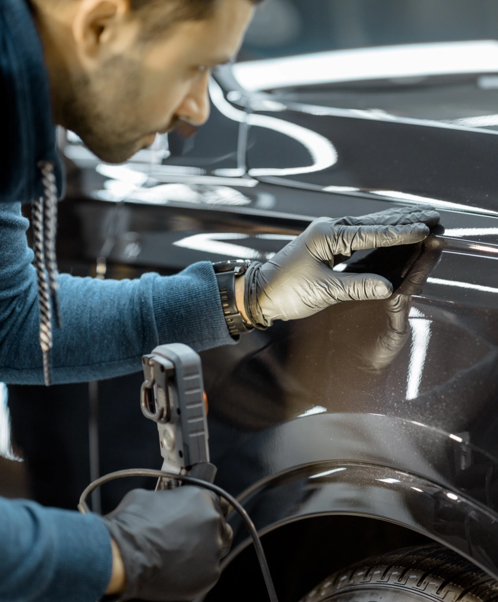 Man in gloves inspecting the polished surface of a black car with a tool in his hand.