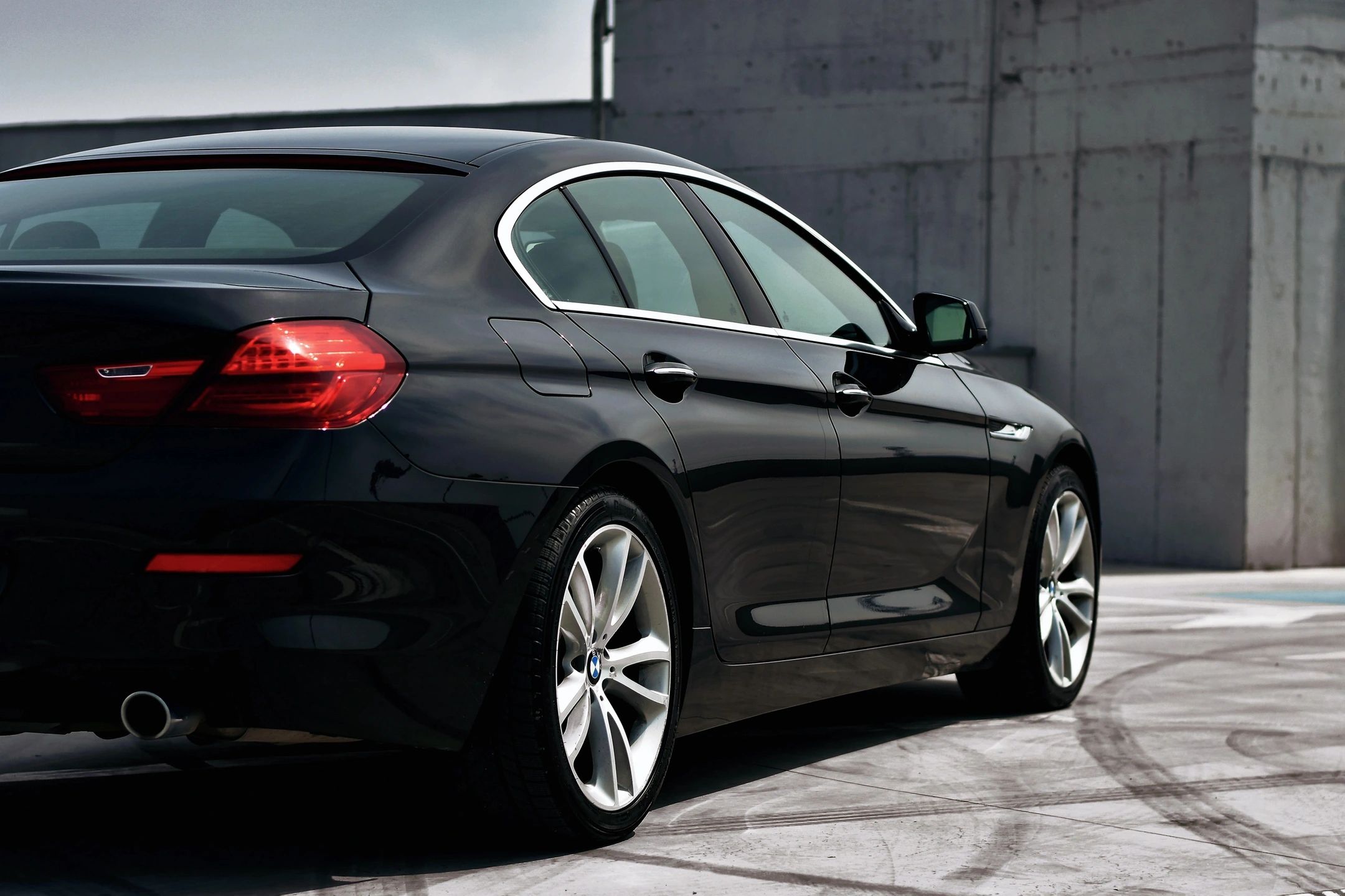 A black car parked in the street near a wall.