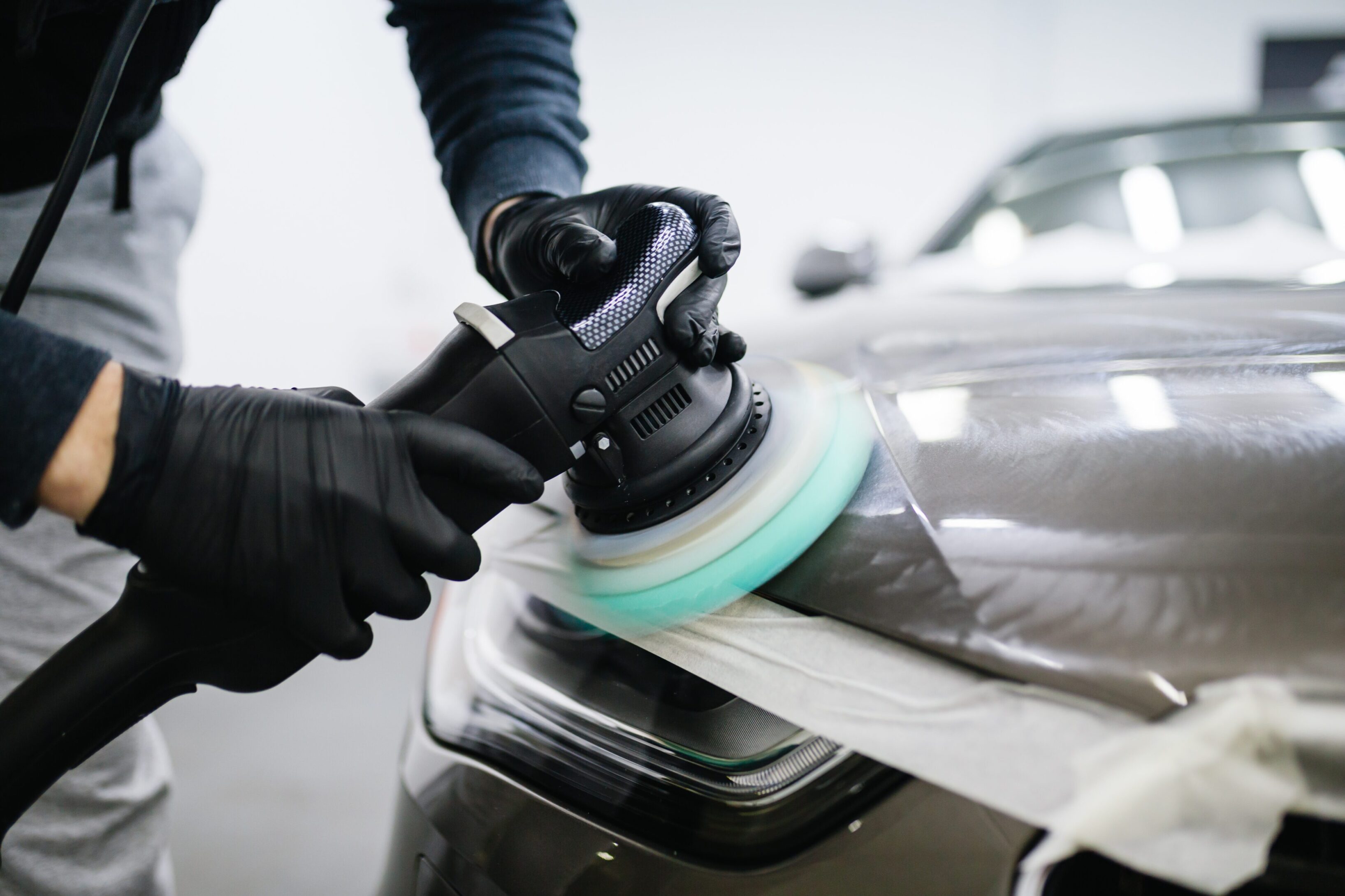 A person is using a polisher on the hood of a car.