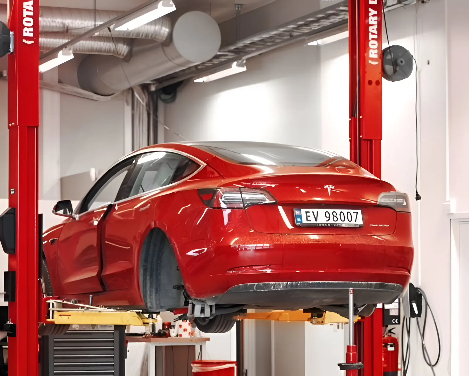 A red car is in the garage and has its hood up.