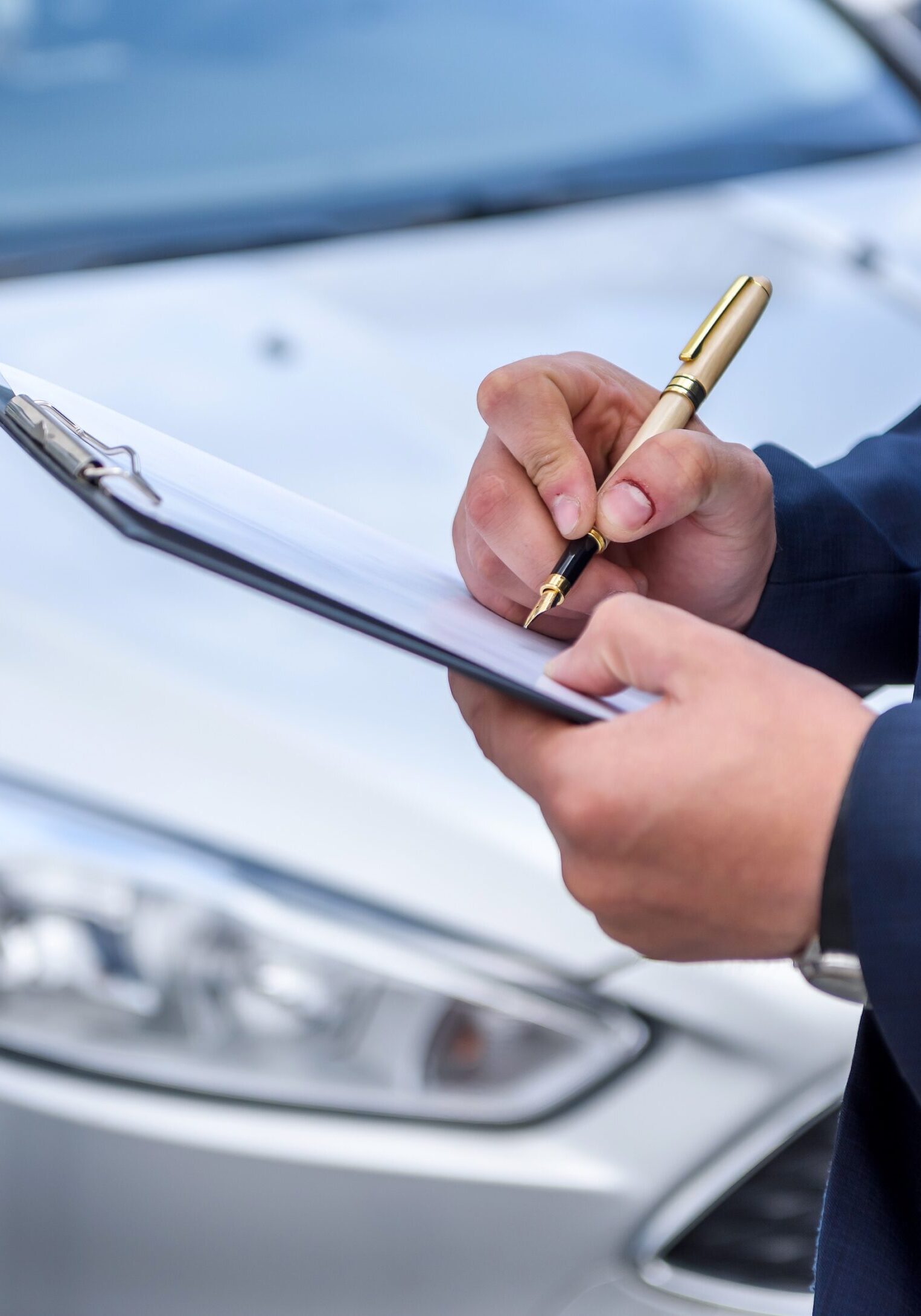 A person writing on paper near a car.